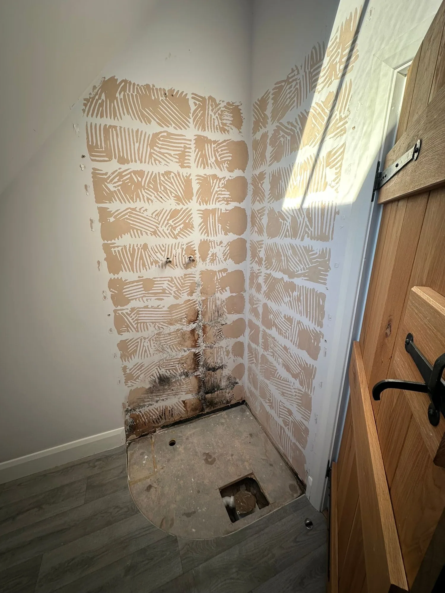 Bathroom mid strip-out with tile adhesive still on the walls, WC waste and supply exposed