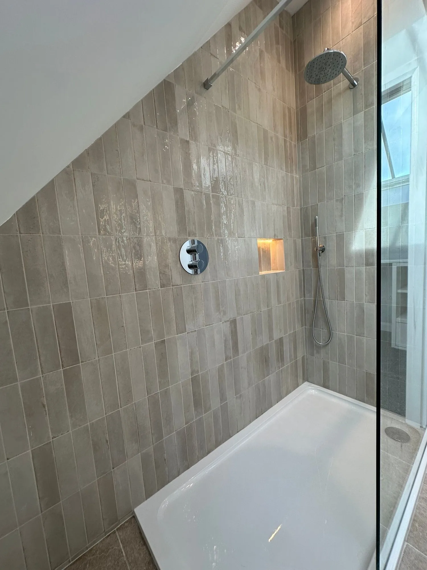 Contemporary walk-in shower with narrow beige tiles, rainhead, handset and lit niche