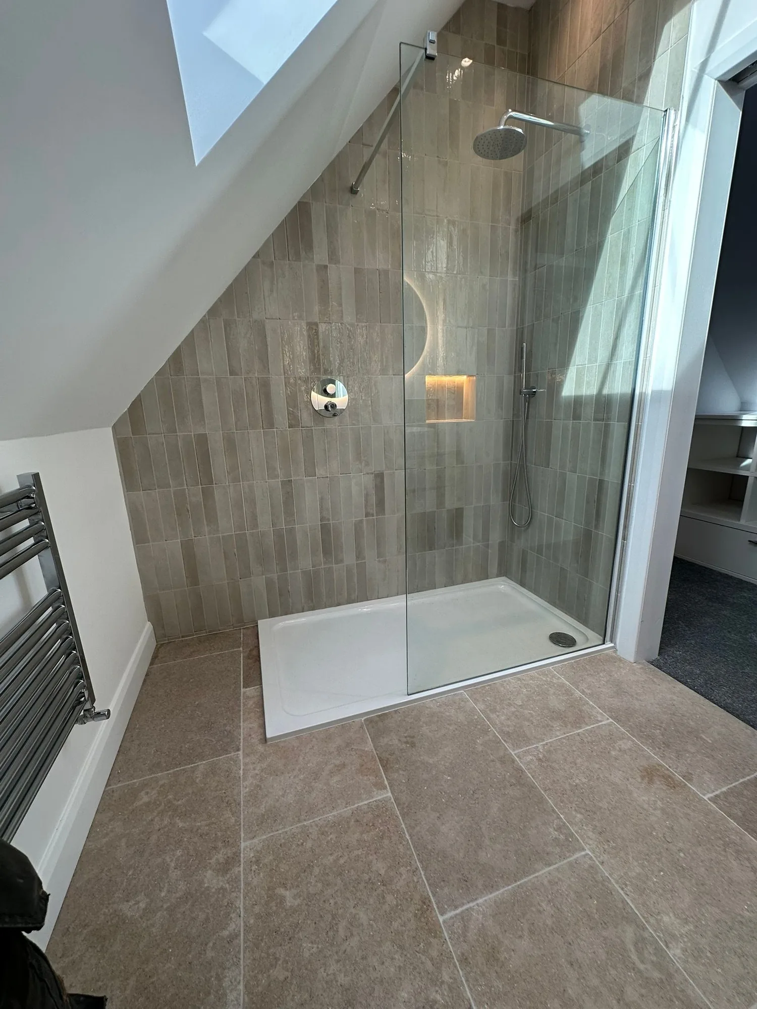 Wider view of the contemporary loft ensuite shower with stone floor and chrome towel rail